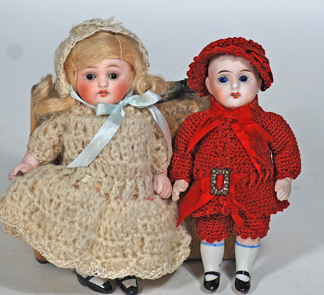 TWO GERMAN ALL-BISQUE DOLLS.: 52. TWO GERMAN ALL-BISQUE DOLLS. Each is all-bisque with glass sleep eyes, painted lashes and brows, open mouth, upper teeth, painted white knee socks and black shoes; 5” doll in crocheted red s