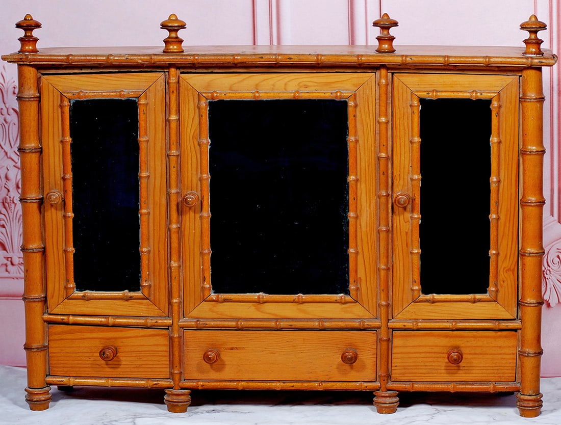 FRENCH MAPLE WOOD DOLL’S ARMOIRE: 21” x 18” Richly-grained maple wood with faux bamboo styling, three mirrored doors, two with interior shelving, wooden door pulls and finials Commentary: Circa 1890, all-original with moderate wea