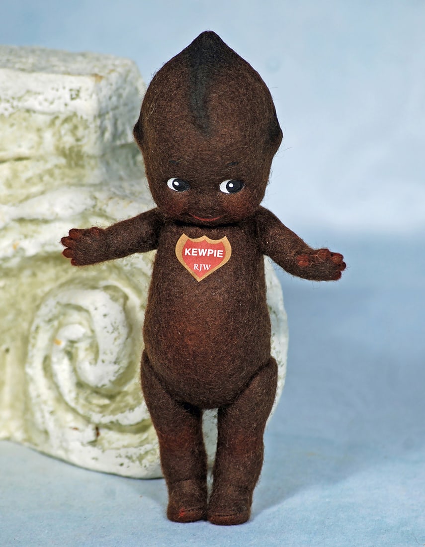 HOTTENTOT KEWPIE BY R: HOTTENTOT KEWPIE BY R. JOHN WRIGHT. 6”. Dark brown pressed felt Kewpie with black side-glancing eyes, swivel head, jointed limbs, blue wings, red heart label on chest. With RJW brass buttons and