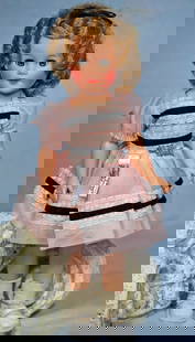 IDEAL 1957 SHIRLEY TEMPLE: 7. IDEAL 1957 SHIRLEY TEMPLE. 14”. Vinyl socket head on five-piece jointed body, sleep eyes, blonde hair in original set, tagged pink nylon dress, white vinyl shoes, Shirley Temple script pin.