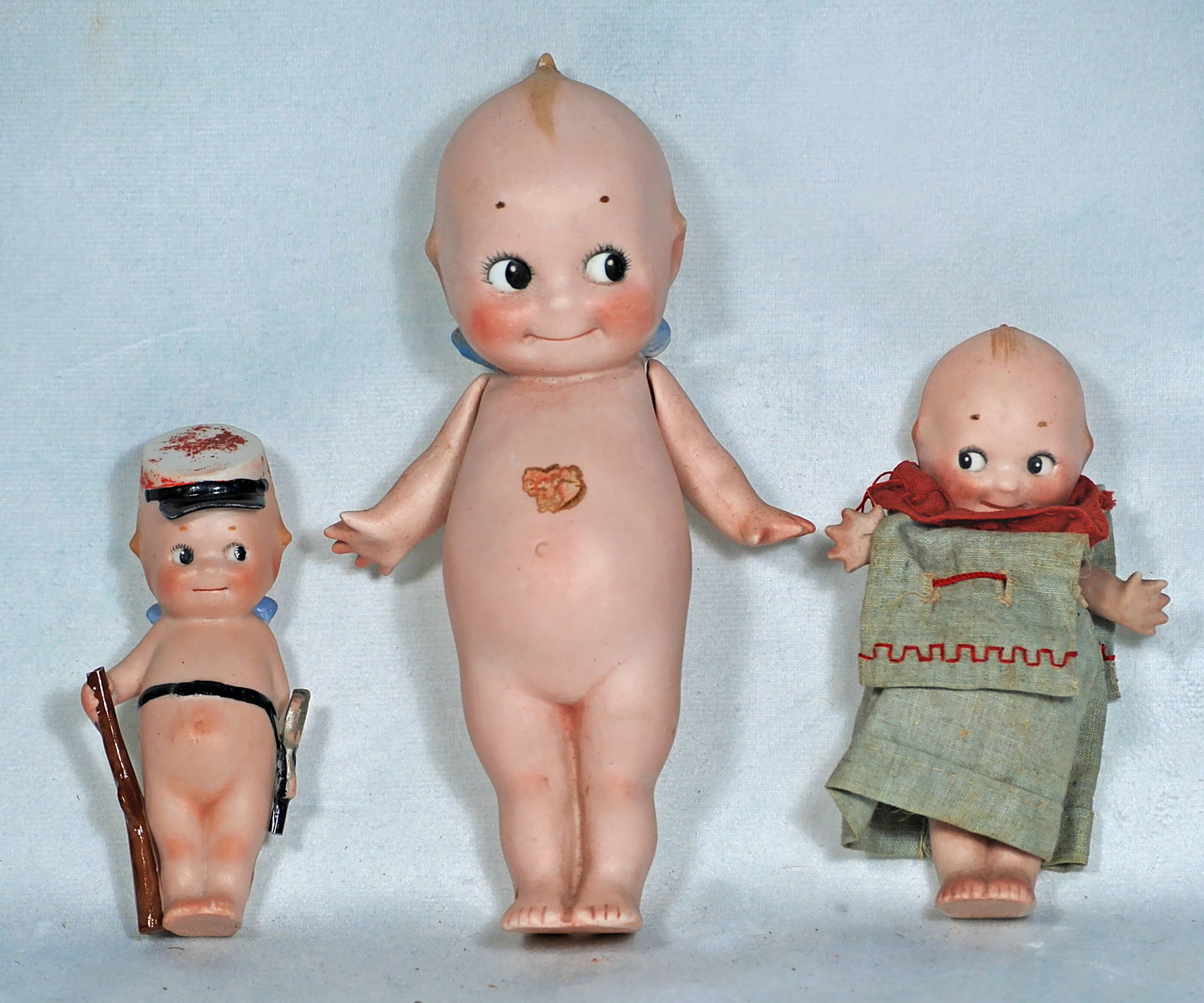 THREE GERMAN BISQUE KEWPIE DOLLS.: 87. THREE GERMAN BISQUE KEWPIE DOLLS. 5 ½” and 7” standing Kewpie, jointed at shoulders, 4 ½” Kewpie solider with sculpted hat, belt with sabre and rifle. Commentary: t