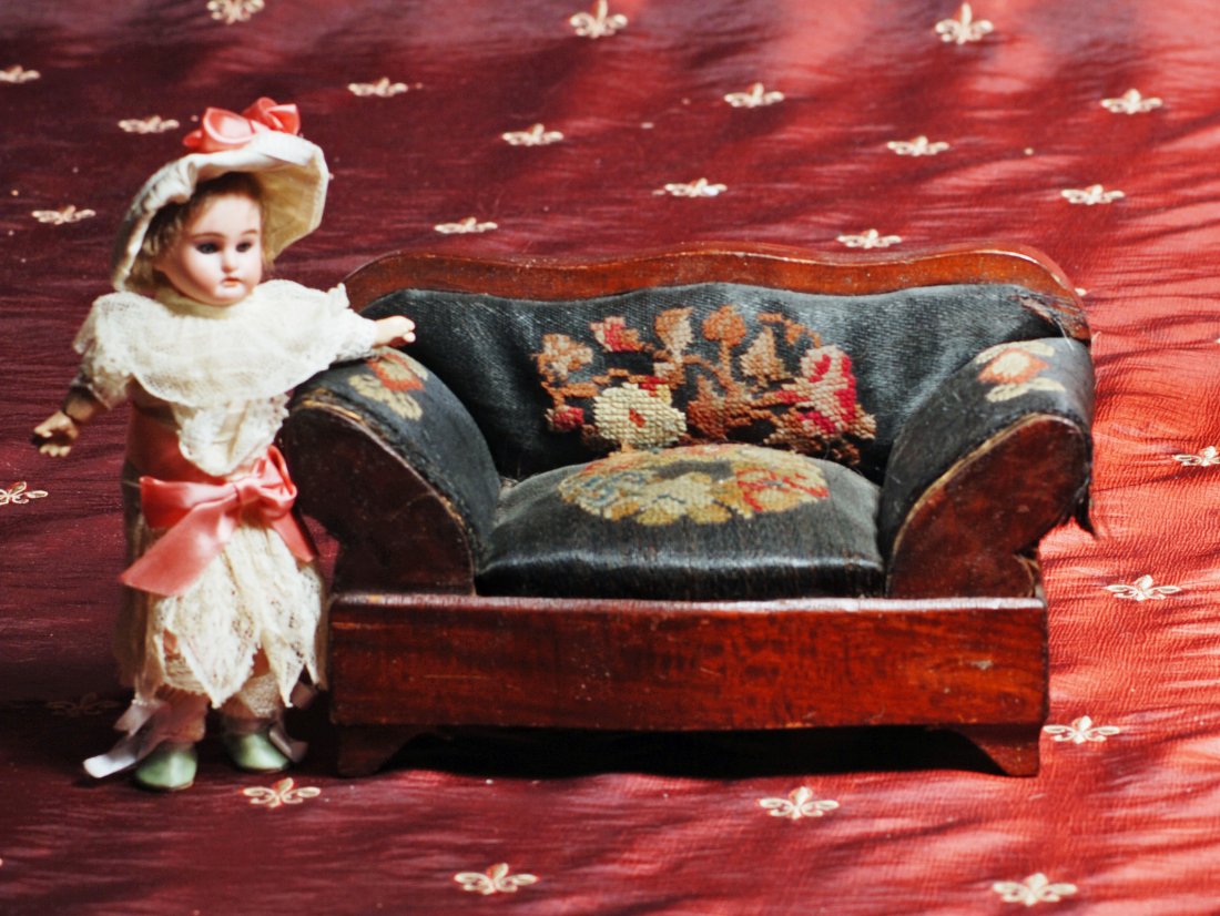 MINIATURE ANTIQUE DOLL’S SOFA: MINIATURE ANTIQUE DOLL’S SOFA. 5” H. x 9” W. Carved walnut sofa with curved back, rolled arms and applied feet; covered in original embroidered black taffeta fabric. Commentary: Moderate fabric 