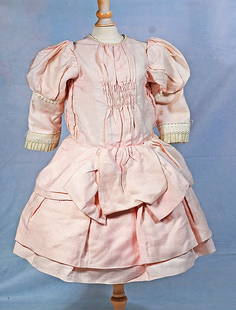 PINK DOLL DRESS: PINK DOLL DRESS. Pale pink cotton dress with puffed sleeves, deep cuffs, lace trimmed front plastron, two-tiered pleated skirt, attached petticoat, 6” shoulder width, 16” length. Commentar