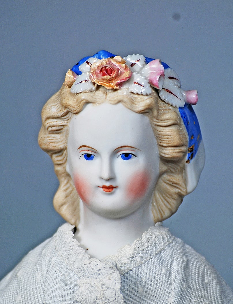 GERMAN BISQUE LADY WITH SCULPTED AND DECORATED BLONDE HAIR: GERMAN BISQUE LADY WITH SCULPTED AND DECORATED BLONDE HAIR. 12 ½”. Bisque shoulderhead. Sculpted blonde hair waved away from face, decorated with Dresden flowers, gilt-trimmed leaves and bl