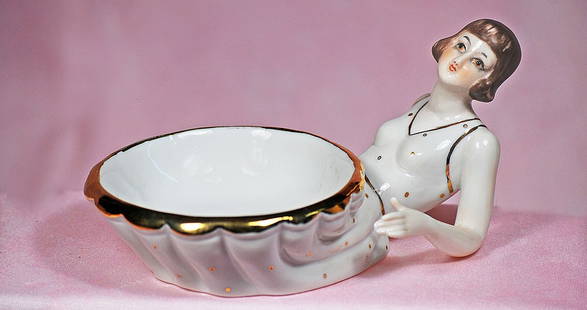 GERMAN PORCELAIN FLAPPER LADY AS CANDY DISH: GERMAN PORCELAIN FLAPPER LADY AS CANDY DISH. 6&#8221; x 3 &#189;&#8221;. All porcelain figure of flapper lady in seated, curled up pose to form a candy dish; having sculpted short brown hair, painted
