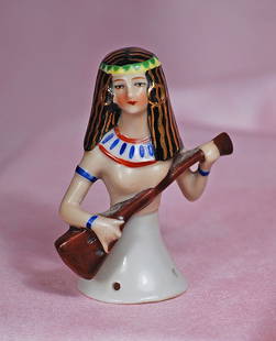 GERMAN PORCELAIN EGYPTIAN THEMED HALF DOLL: GERMAN PORCELAIN EGYPTIAN THEMED HALF DOLL. 3”. Marks: Germany. Waist-up porcelain half figure depicting a Egyptian lady with long black hair with gilt accents plus green and white headband,