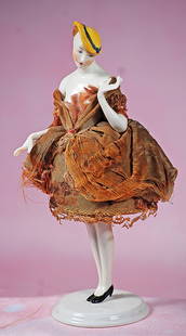 GERMAN PORCELAIN HALF DOLL IN YELLOW BONNET WITH PORCELAIN LEGS: GERMAN PORCELAIN HALF DOLL IN YELLOW BONNET WITH PORCELAIN LEGS. 7 ½”. Waist-up porcelain figure of slender-bodies lady, head tilted to the side, yellow bonnet over short brown hair,