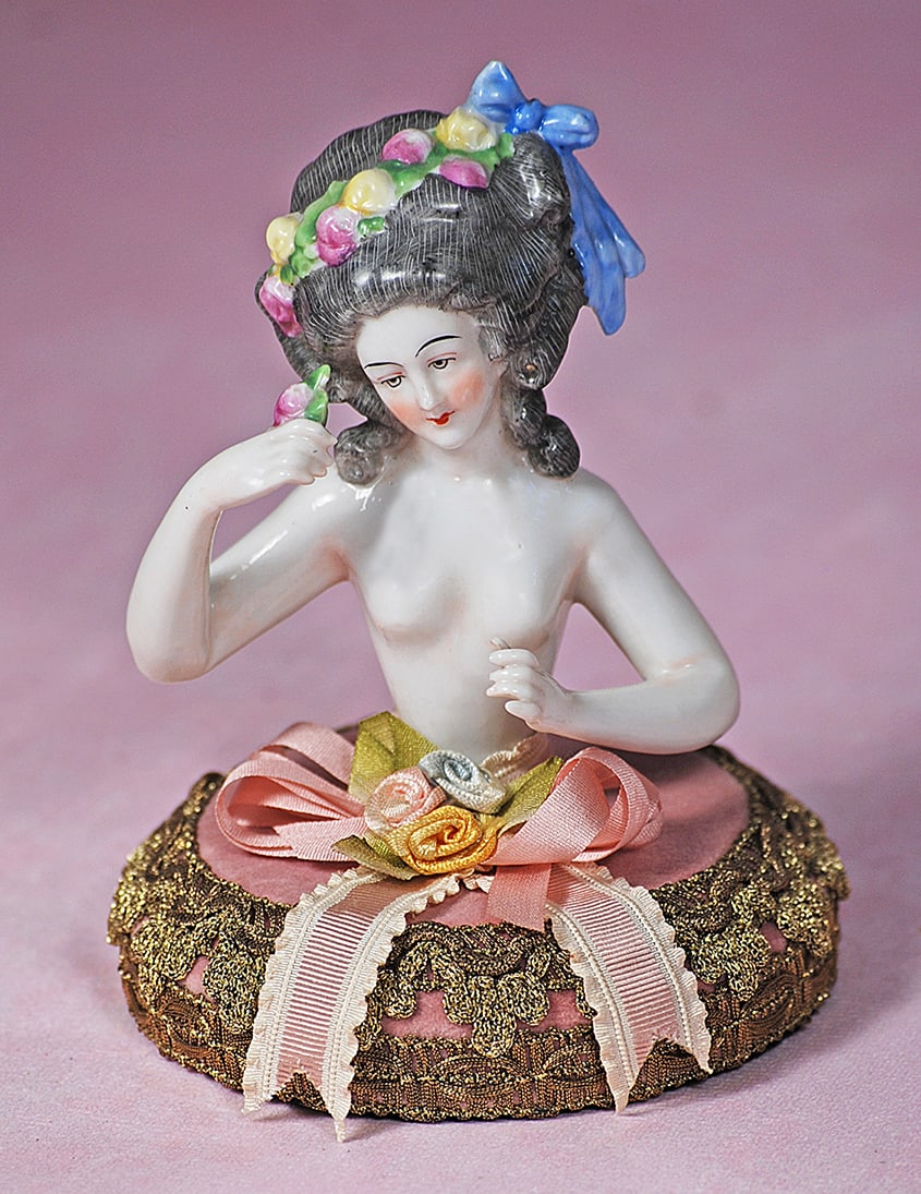 GERMAN PORCELAIN HALF DOLL WITH ELABORATE COIFFURE: GERMAN PORCELAIN HALF DOLL WITH ELABORATE COIFFURE. 4”. Waist-up nude figure of lady with sculpted gray hair in elaborate arrangement and decorated with garland of flowers and blue bow, painted 