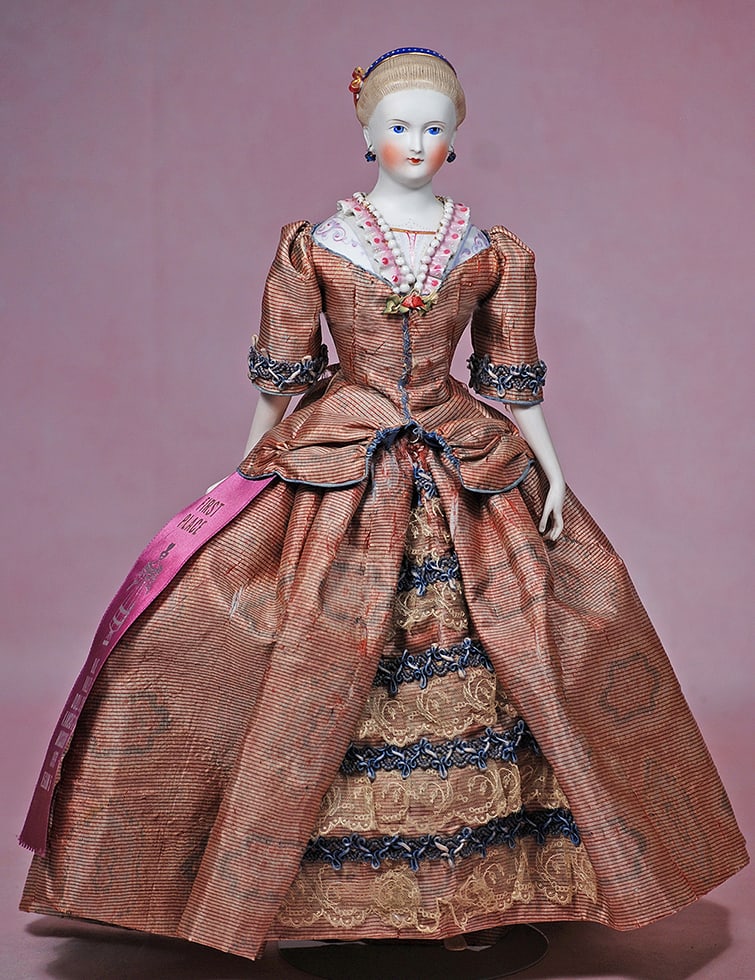 GERMAN BISQUE LADY WITH SCULPTED HAIR ORNAMENTS AND BODICE: GERMAN BISQUE LADY WITH SCULPTED HAIR ORNAMENTS AND BODICE. 15”. Bisque shoulderhead with pale complexion, blonde sculpted hair drawn from face, decorated by a gilt-edged royal blue hair band wi