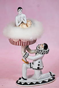 GERMAN PORCELAIN POWDER DISH AND PUFF WITH KNEELING PIERROT: GERMAN PORCELAIN POWDER DISH AND PUFF WITH KNEELING PIERROT. 9 &#189;&#8221;. Marks: 6084. Two-piece ensemble features an oval porcelain base with stylized Art Deco geometric designs upon which a clas
