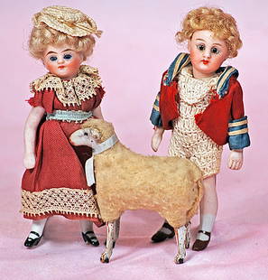 TWO MINIATURE ALL-BISQUE MIGNONETTES WITH WOOLY LAMB: TWO MINIATURE ALL-BISQUE MIGNONETTES WITH WOOLY LAMB. 4 ¼”. Each is all-bisque with swivel head, five-piece jointed bisque body, painted shoes and socks, inset glass eyes, painted brows,