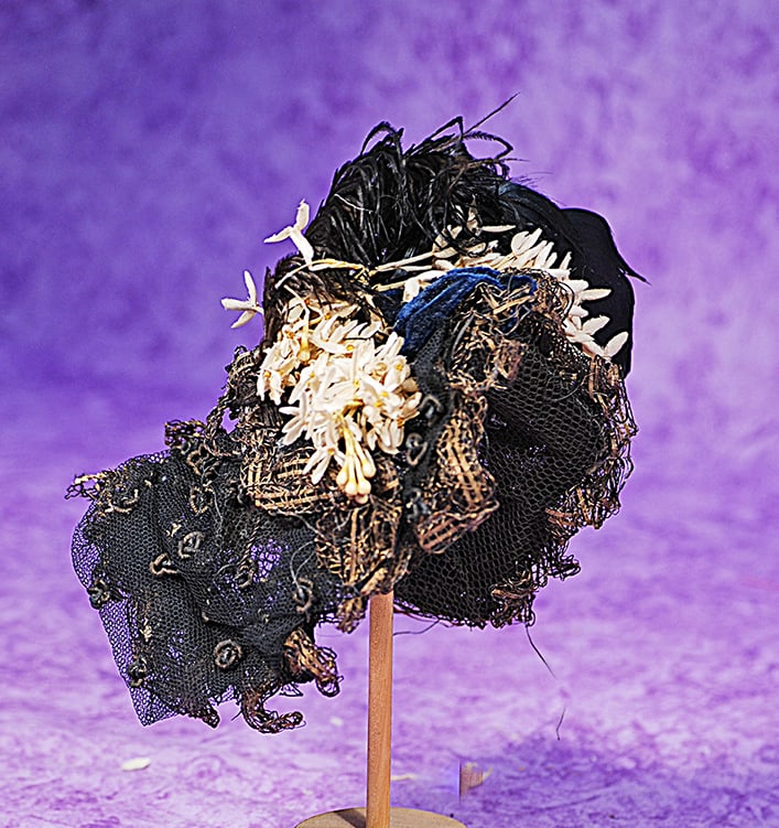 BLACK SILK AND LACE DOLL BONNET.: BLACK SILK AND LACE DOLL BONNET. Wire-framed bonnet covered in black lace over tulle with brown accents, black plume and cream floral sprays, sized for approximately 10” head circumference.
