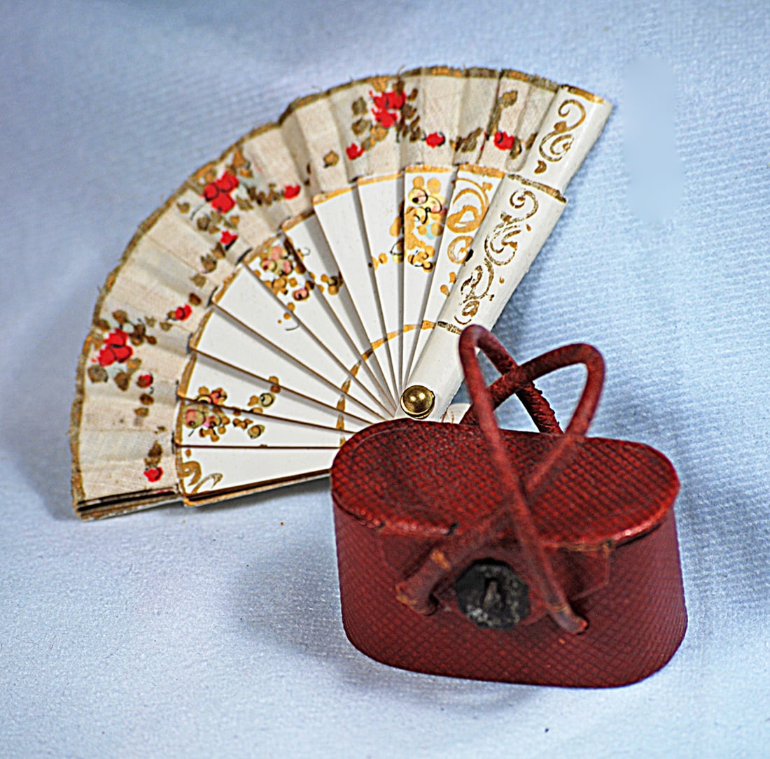 MINIATURE DOLL’S FAN AND FRENCH KIT DE MANUCURE:  2 ¼” celluloid fan with gilt decorations and floral silk border. 1 ¾” x 1” firm-sided red leather case with hinged top and leather handles and containing