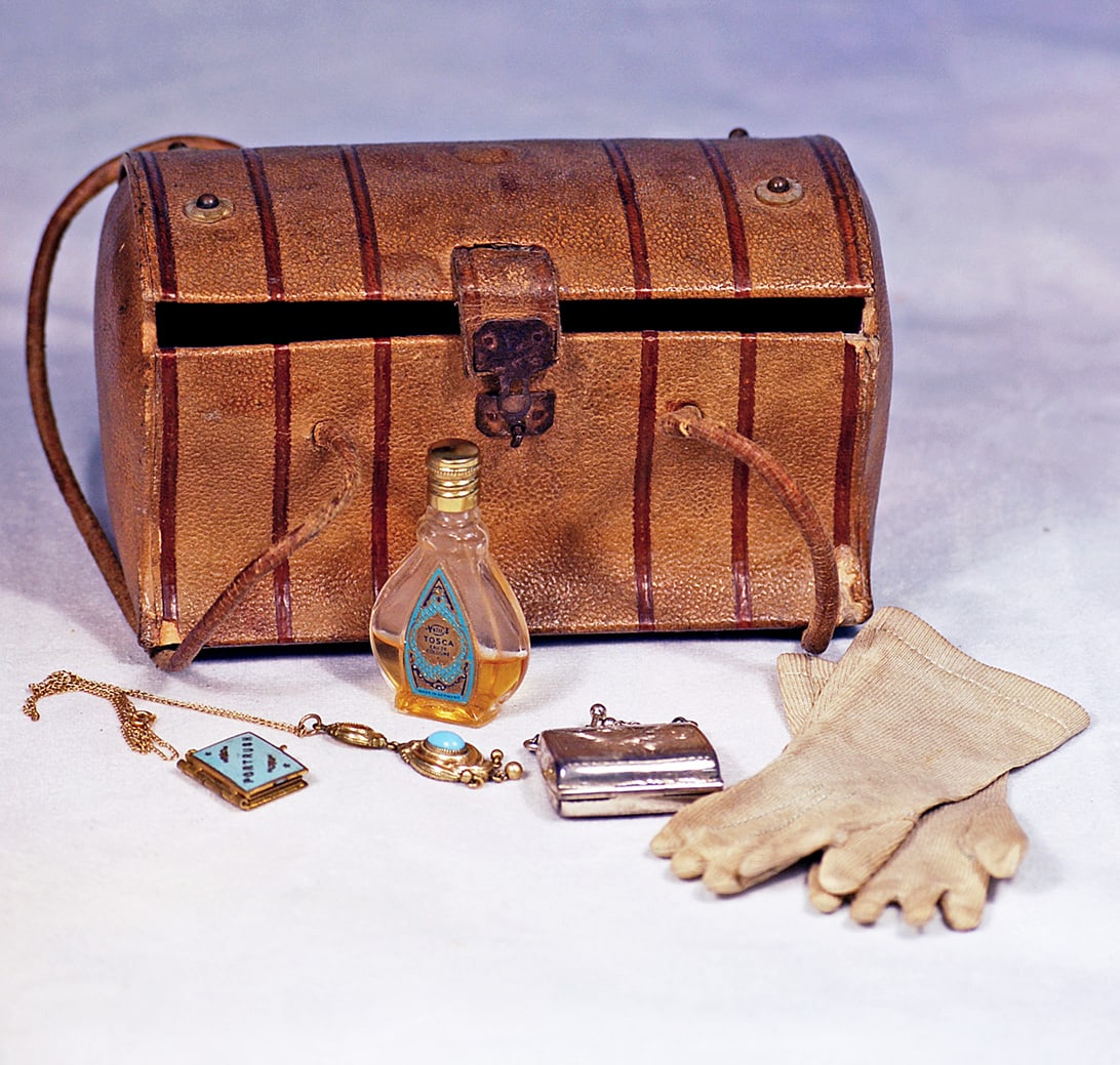 FRENCH TRAVEL VALISE FOR POUPEE: Heavy, shaped cardboard valise with leather skin covering, metal latch, leather handles, magenta paper-lined interior; plus miniature silver purse, necklace, perfume decanter, and gloves.