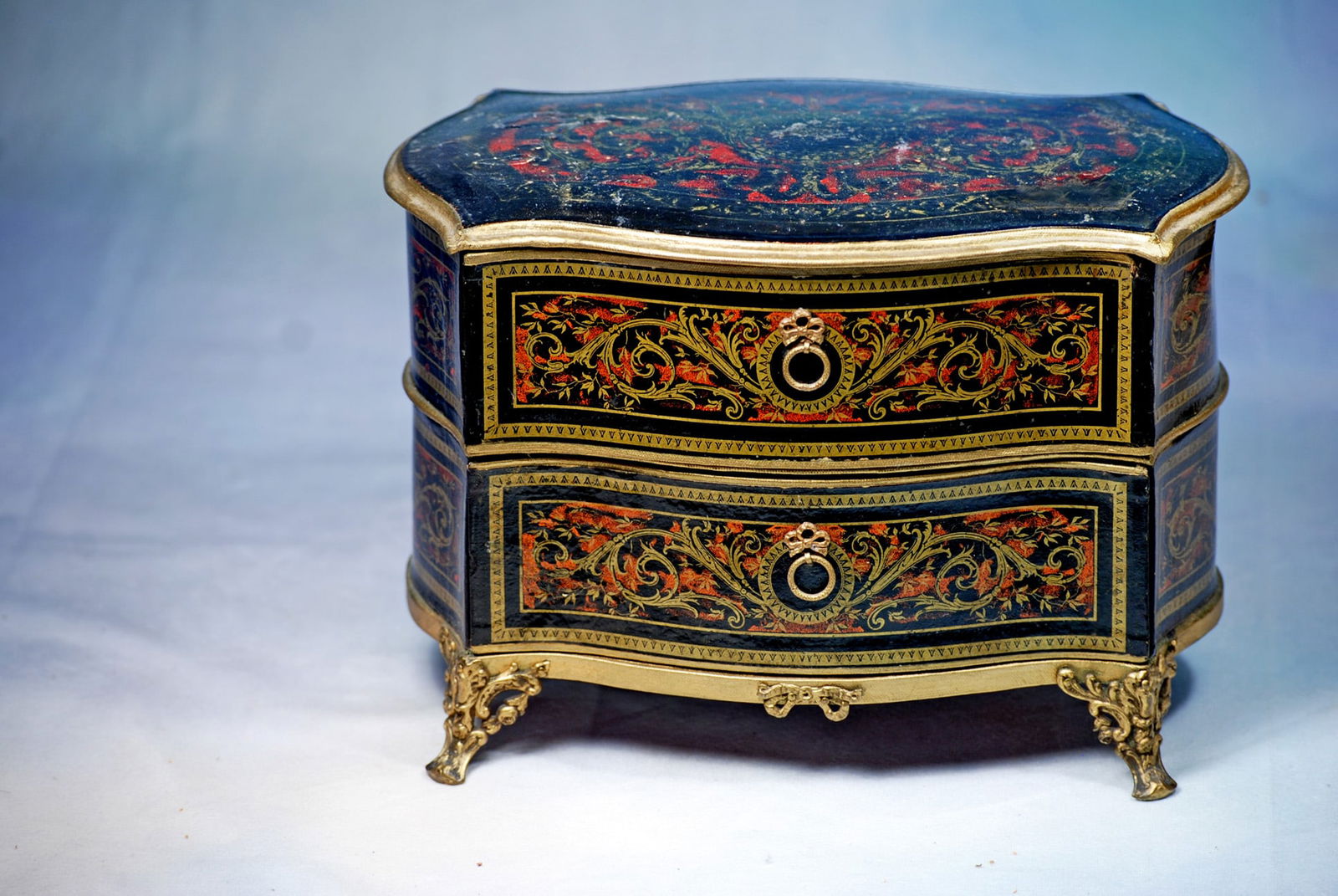 FRENCH MINIATUARE CHEST OF DRAWERS IN THE BOULLE STYLE:  9” W. x 6 ½” H. Firm-sided heavy card stock, two drawers, curved bombe front, sides and back with shaped top; original lithographed paper cover to simulate inlay designs