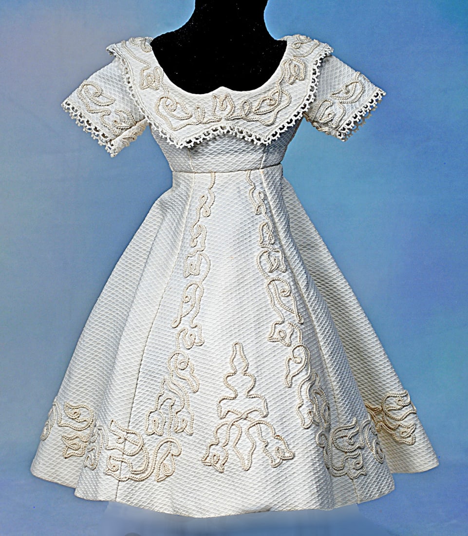 WHITE WOVEN COTTON MODE ENFANTINE GOWN: Cotton pique gown featuring dart-shaped bodice, low rounded neckline with collar and short sleeves; soutache and lace trim detail on sleeves and collar; flared skirt with elaborate soutache trim,