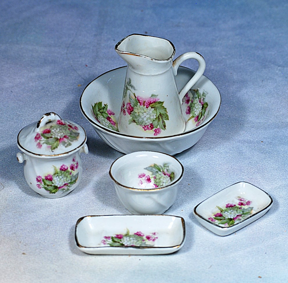 TINY GERMAN PORCELAIN MINIATURE TOILETTE SET: 2 ¾” pitcher. White porcelain wash set has dainty pastel floral and greenery designs and gilt edging, and includes pitcher, wash bowl and smaller bowl plus two rectangular trays, and