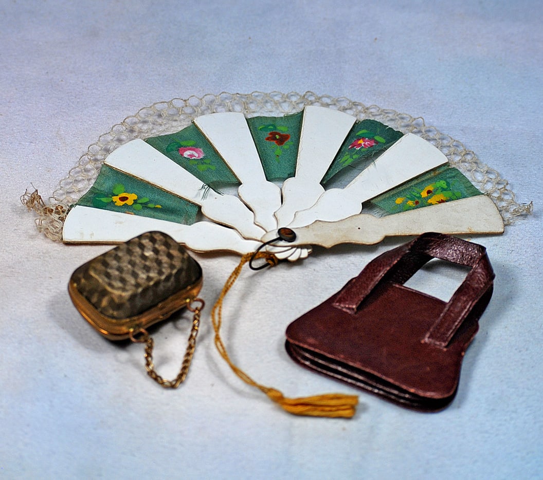 DOLL ACCESSORIES: 3” white celluloid folding fan with green silk print fabric and lace edging; 1 ½” embossed metal doll purse with link-chain; 2” dark maroon leather purse with leather