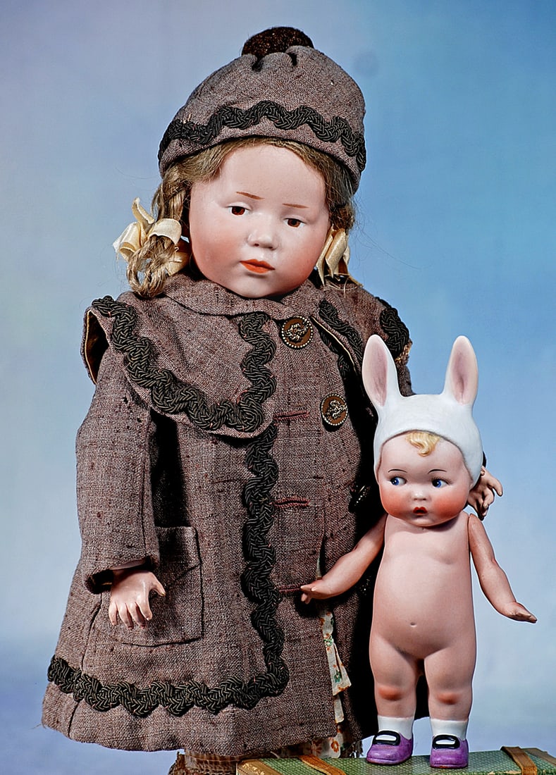 GERMAN ALL-BISQUE CHARACTER IN BUNNY HAT: 7 ½”. Marks: Germany (on foot). All-bisque character jointed at shoulders, sculpted white hat with bunny ears over blonde forelock, painted side-glancing googly eyes, upper lashes,