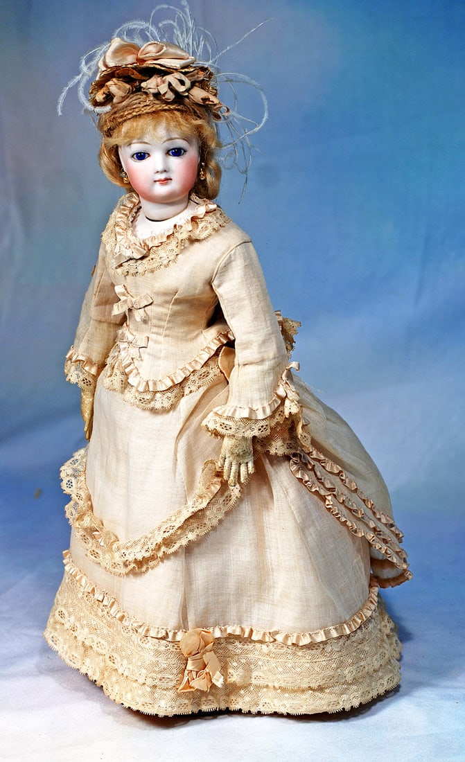 FRENCH BISQUE POUPEE IN ORIGINAL GOWN: 14”. Marks: None visible. Bisque swivel head on bisque shoulderplate, blue paperweight eyes, painted lashes, eyeliner, feathered brows, pierced ears, closed mouth, accented lips, blo