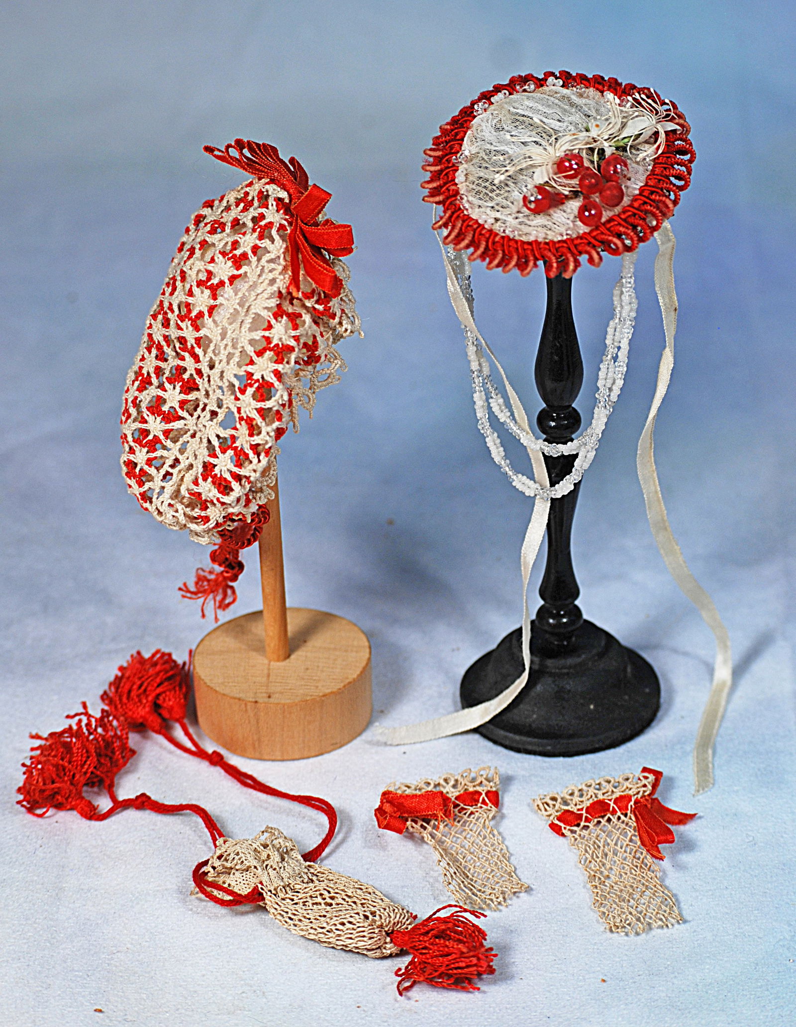 DOLL BONNETS AND ACCESSORIES: Hand-netted accessories garnished with red ribbons, cords, and tassels of red silk; plus a fancy little bonnet or ruched gauze bordered in coils of wired red silk, accented with berries and