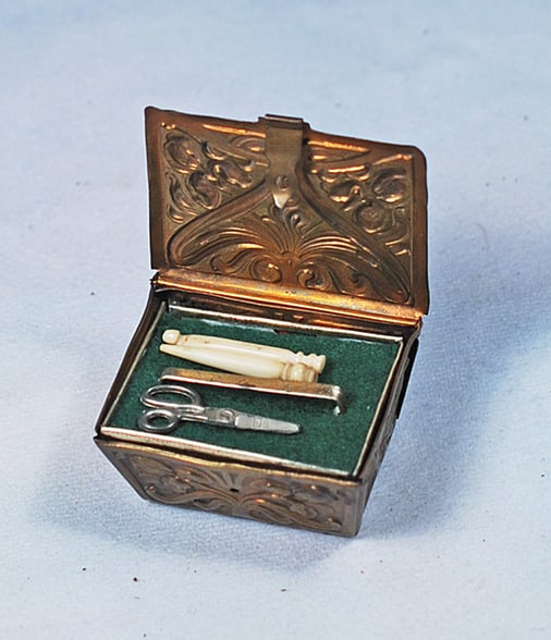 MINIATURE EMBOSSED METAL FITTED SEWING NECESSAIRE:  2” x 1” embossed metal case with clasp contains a green felt-lined tray with various bone-handled sewing implements and below the tray a tiny spool of thread and metal thimble.