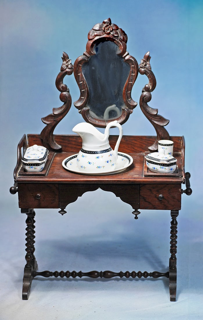 SUPERB FRENCH WOODEN VANITY TABLE WITH PORCELAIN TOILETTE SET: 16” H. x 9 ½” W. Dark walnut vanity table with wooden framed mirror and fancily carved side supports, two towel bars, decorative finials; plus porcelain toilette set comprising