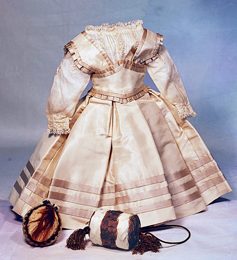 FINE, STYLISH ENSEMBLE FOR POUPEE: Features a cream silk taffeta gown with wide waistband that forms a bodice with wide straps, box-pleated skirt, trimmed with bands of satin ribbon, further accented with pleated ruches, back hook-eye