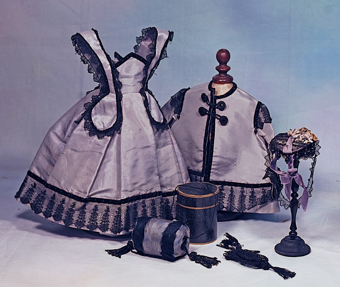 LOVELY, STYLISH LAVENDER SILK ENSEMBLE FOR POUPEE: Featuring a gown of beautiful lavender silk with high pointed waistband, bretelles descending into rounded lappets in front and back, edged round with Chantilly lace and black velvet studded with jet;