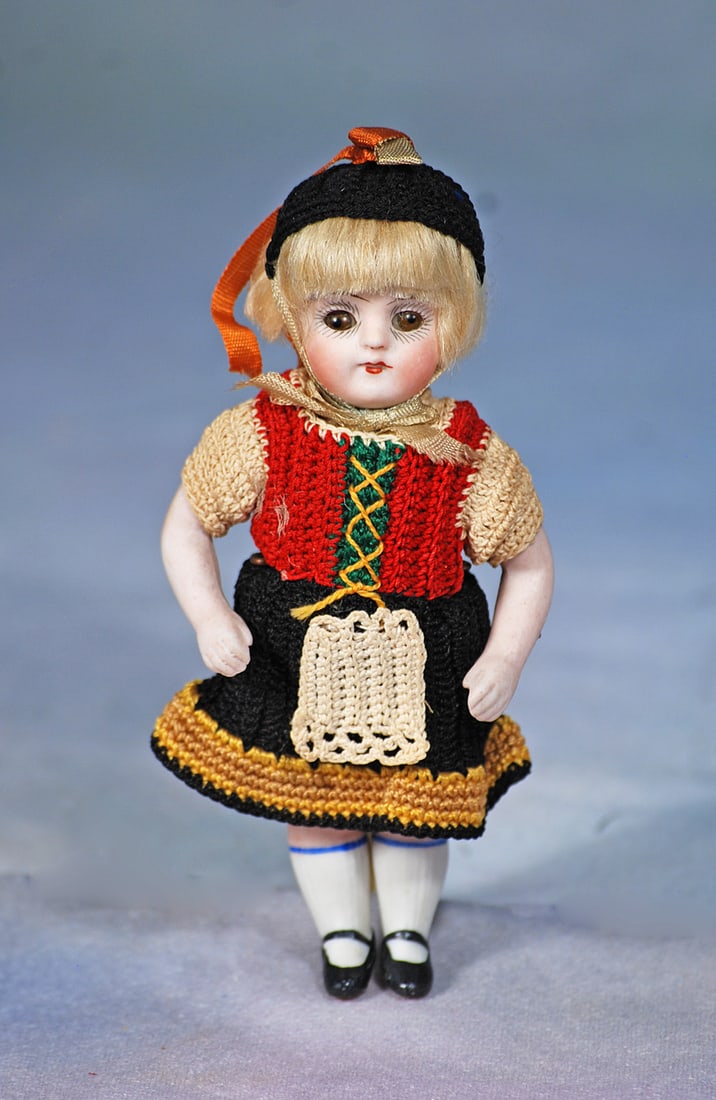MINIATURE GERMAN BISQUE DOLL BY KESTNER IN ORIGINAL COSTUME: 5”. Marks: 257. All-bisque, jointed at shoulders and hips, brown sleep eyes, painted lashes, tapered brows, closed mouth, painted knees socks and black shoes, original blonde mohair
