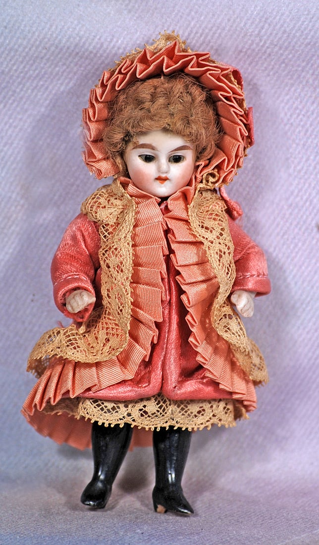 TINY GERMAN ALL-BISQUE MIGNONETTE: 4”. All-bisque doll jointed at shoulders and hips, stationary brown glass eyes, tapered brows, closed mouth, curly light-brown mohair wig, painted black knee stockings and black heeled sho