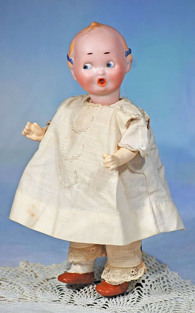 GERMAN BISQUE GOOGLY WITH BLUE HAIR BOWS BY RECKNAGEL: 7”. Marks: R 50 A 10/0. Bisque socket head, painted brown hair with defined curls over the ears accented with blue hair bows, painted features, large round blue side-glancing eyes, p