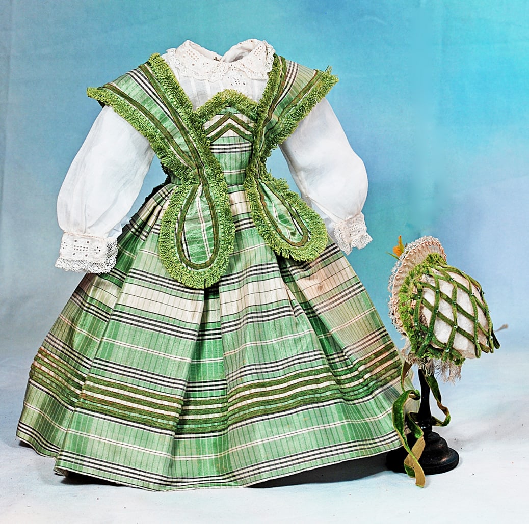 GREEN AND WHITE SILK GOWN AND BONNET FOR POUPEE: Features a cream silk taffeta gown with wide waistband that forms a bodice with wide straps, box-pleated skirt, trimmed with bands of narrow green velvet and coordinating silk fringe, rounded lappets