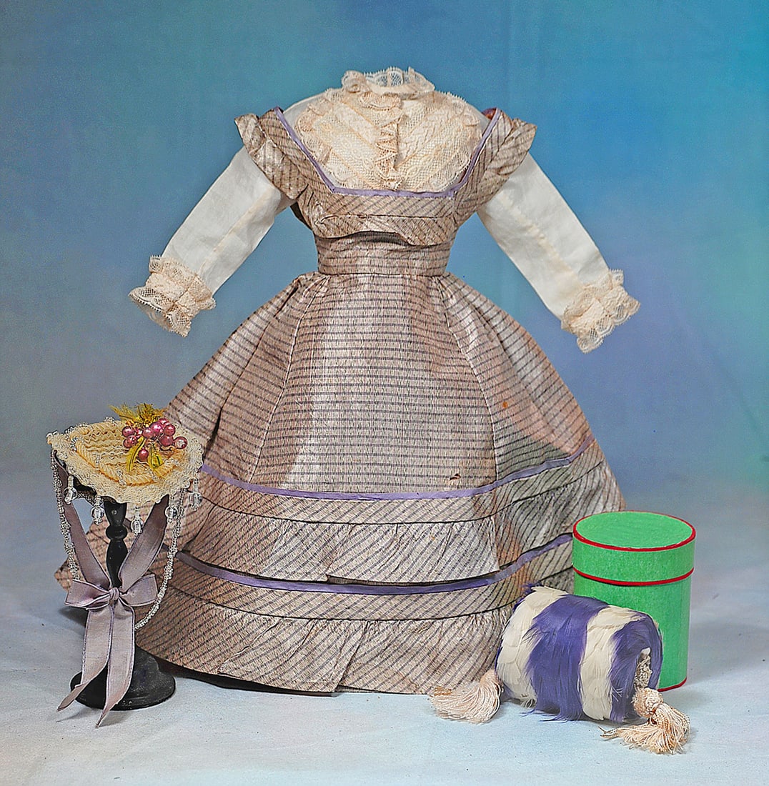 LILAC AND MAUVE SILK ENSEMBLE FOR POUPEE: Features a mode enfantine style gown of intermingled lilac and mauve silk with bias-cut flounces decorating the skirt and bodice, gathered skirt with fullness at back, hook-eye closing; white muslin