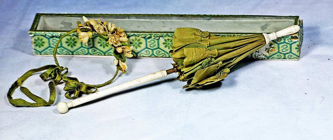 GREEN SILK DOLL PARASOL WITH BONE HANDLE AND ORIGINAL BOX, WITH FLORAL AND WAX GARLAND: 10” Green silk parasol with ruffled and pinked edges, metal fittings, bone handle and finial, factory original box. Plus a garland decorated with waxed flowers with green accents,