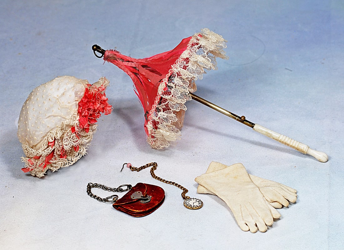 SELECTION OF DOLL ACCESSORIES: Comprising a 14” pagado-style rose-pink silk parasol with gathered lace edging, carved bone handle, metal fittings, tip and loop; a dainty white dotted swiss cap with lace ruffled edge, rose-pin