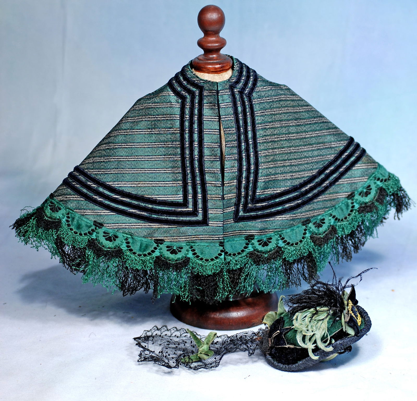 SILK CAPE AND VELVET BONNET FOR POUPEES: Fine green silk cape is trimmed all around with crinkled fringe in green and black with green scalloped heading, further accented with three rows of narrow black velvet; plus a bonnet of shaped dark