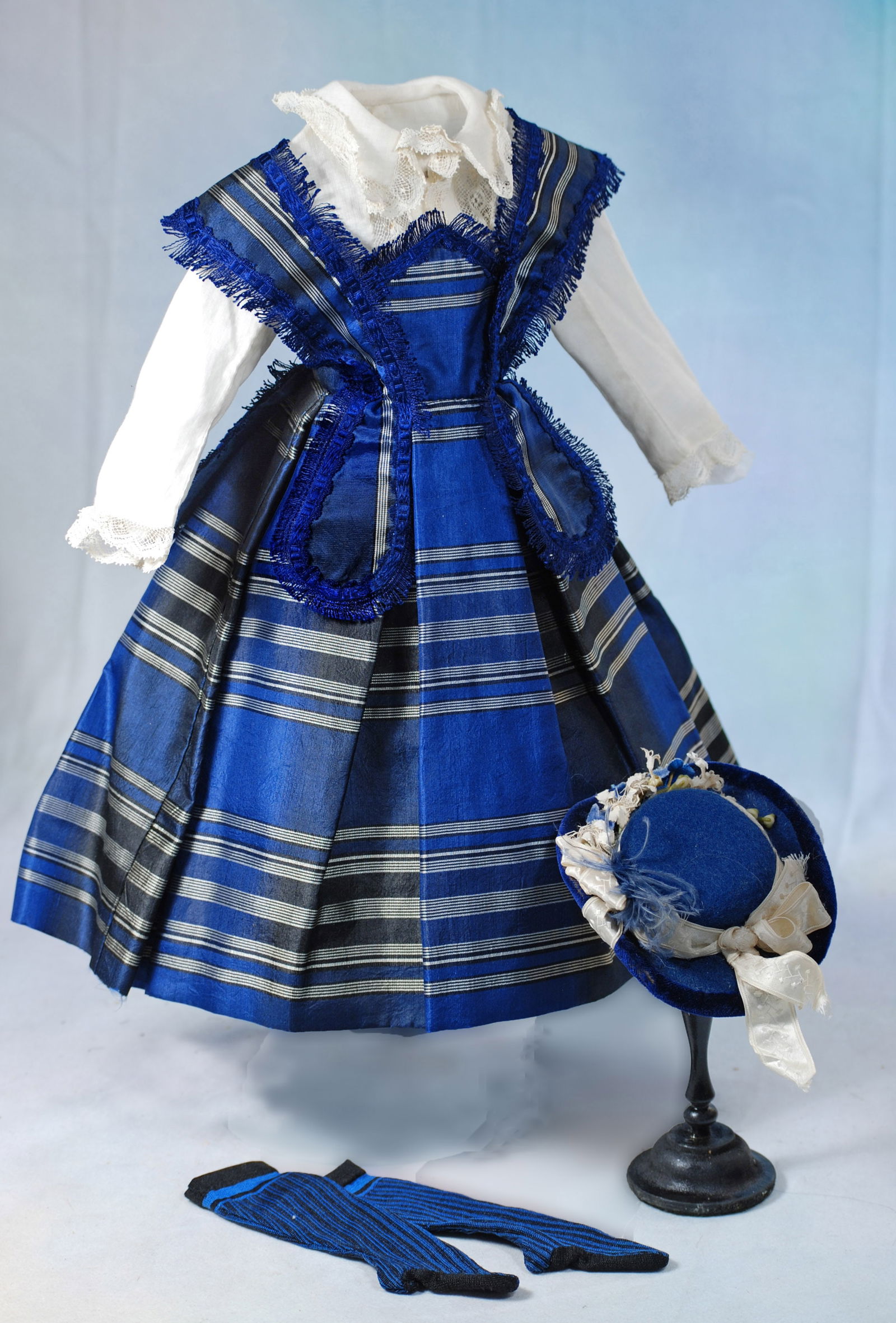 BLUE SILK TAFFETA ENSEMBLE FOR POUPEE: Features a white cotton shirt over a vibrant blue silk taffeta gown shaded with silvery white and black bands, bretelles set over a pointed high waistband and extending over the back falling int