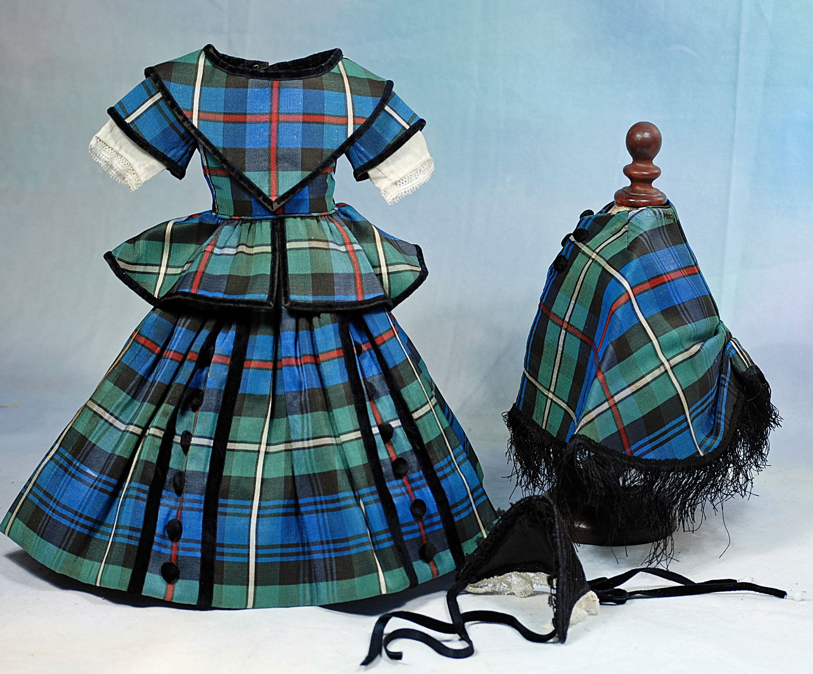 PLAID ENSEMBLE FOR FRENCH POUPEE: Comprising a fitted bodice with v-shaped collar, peblum, short sleeve with white cotton under sleeves, full gathered skirt, bodice edged in narrow black velvet, skirt has black velvet buttons bordered