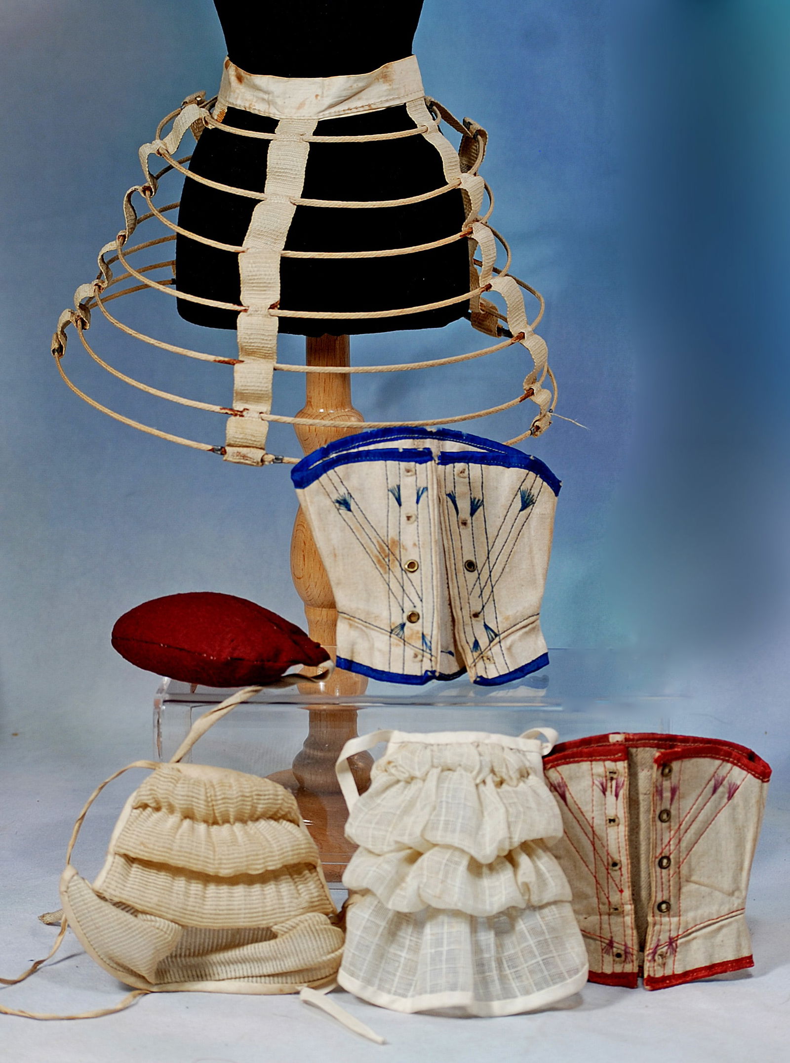 ASSORTED BUSTLES, HOOPS AND CORSETS FOR POUPEE OR LADY DOLL: 257. ASSORTED BUSTLES, HOOPS AND CORSETS FOR POUPEE OR LADY DOLL. Including 8 ½” petticoat hoop; two corsets for 6” to 7” waist, three assorted bustles with waist ties.