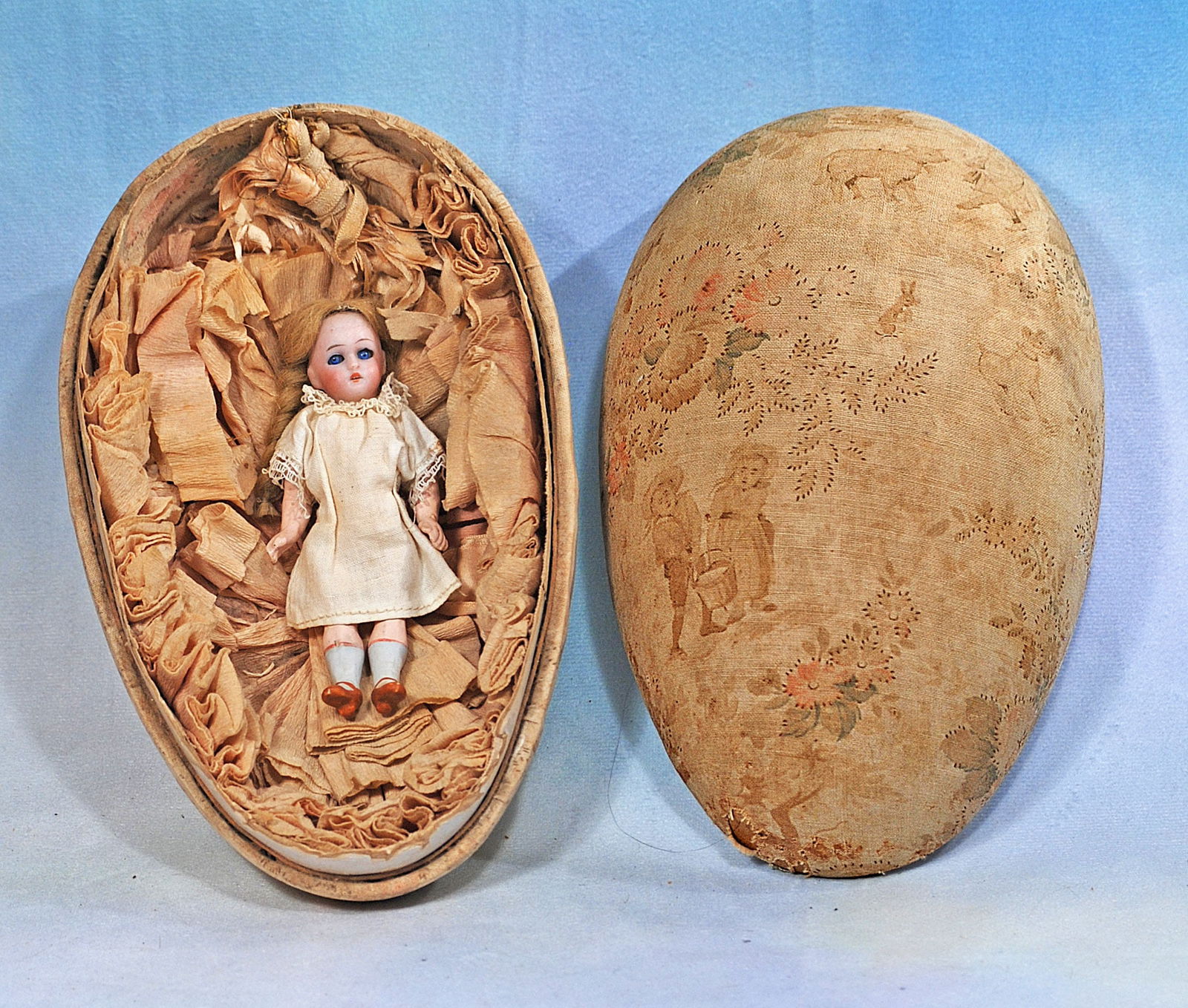 PETITE GERMAN BISQUE DOLL IN SILK COVERED EGG.: 261. PETITE GERMAN BISQUE DOLL IN SILK COVERED EGG. 4 ½” doll; 8” egg. Silk floral and pastel covering over heavy cardboard egg with thickly gathered silk interior holds a