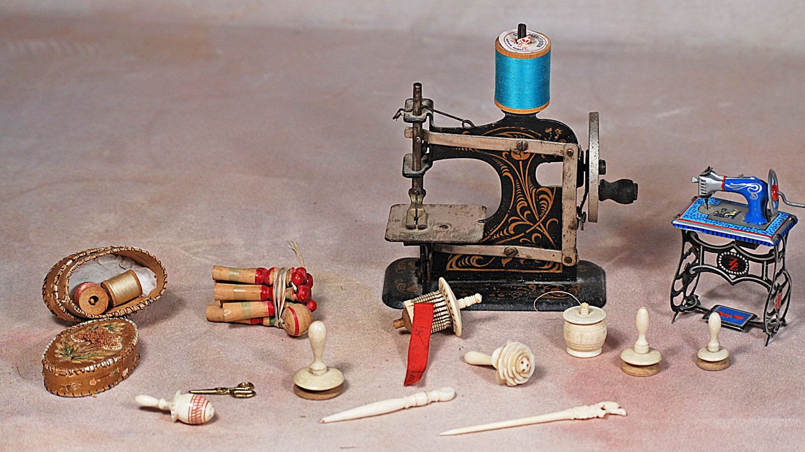 TWO MINIATURE SEWING MACHINES AND ANTIQUE SEWING TOOLS.: 72-A. TWO MINIATURE SEWING MACHINES AND ANTIQUE SEWING TOOLS. 3 ¼” and 4” miniature metal sewing machines; wooden lace making bobbins, tiny scissors, oval box with two spools of