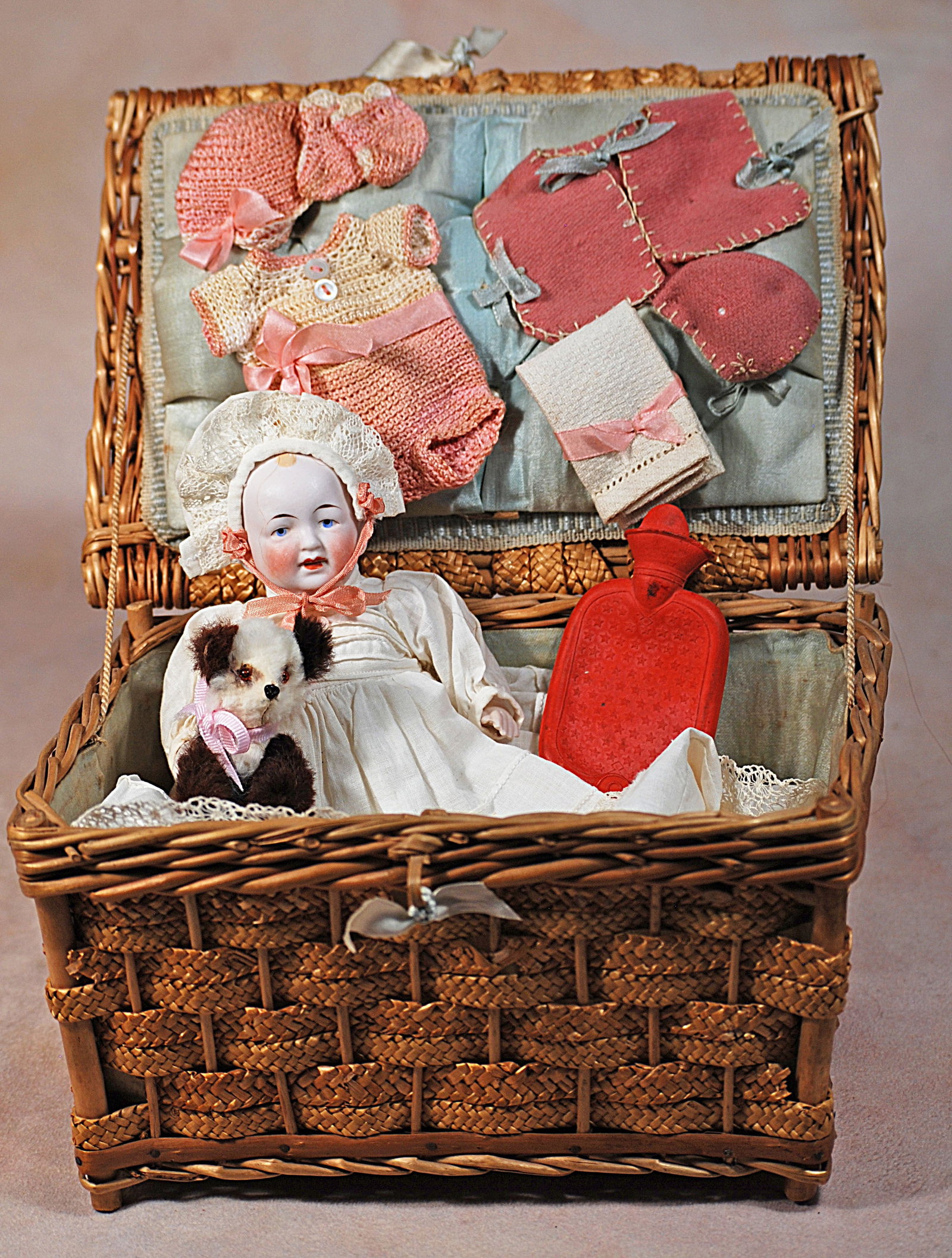 GERMAN ALL-BISQUE BABY WITH LAYETTE.: 75. GERMAN ALL-BISQUE BABY WITH LAYETTE. 7” German all-bisque character baby with painted hair and features, white cotton dress and bonnet; resting in a woven wicker basket with layette, hot