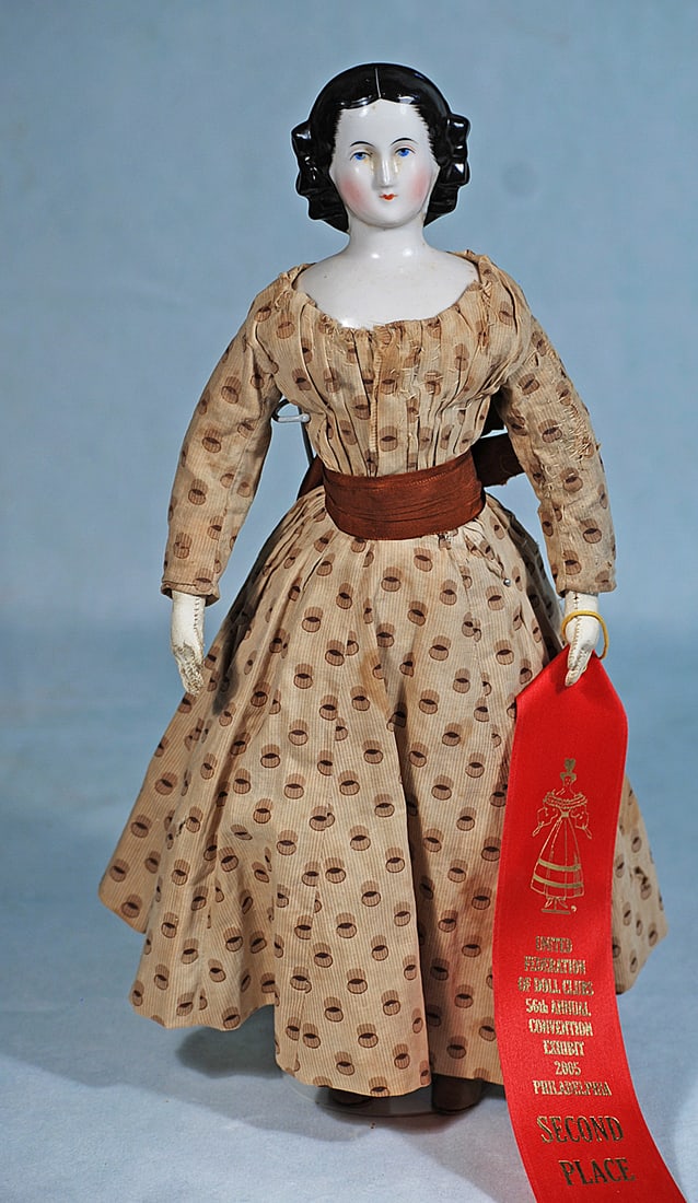 GERMAN PORCELAIN LADY WITH SCULPTED BLACK HAIR AND SNOOD: 14”. Porcelain shoulderhead with sculpted black hair has headband, bow at each side of head, brush marked detail, snood covering the back, painted features, blue eyes, red and black eyeliner, ta