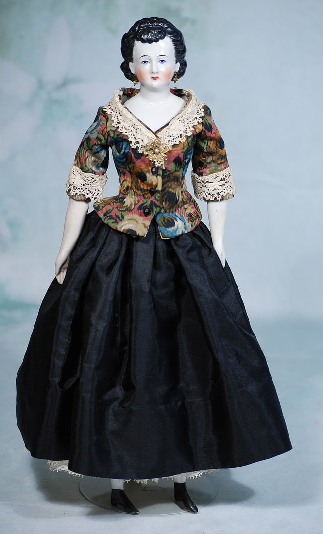 GERMAN PORCELAIN LADY WITH PIERCED EARS AND ORNATE COIFFURE: 16”. Porcelain shoulderhead with black sculpted hair with curly bangs. Hair waved away from face and arranged in pouf of curls then drawn behind the pierced ears into a cluster of curls at the b