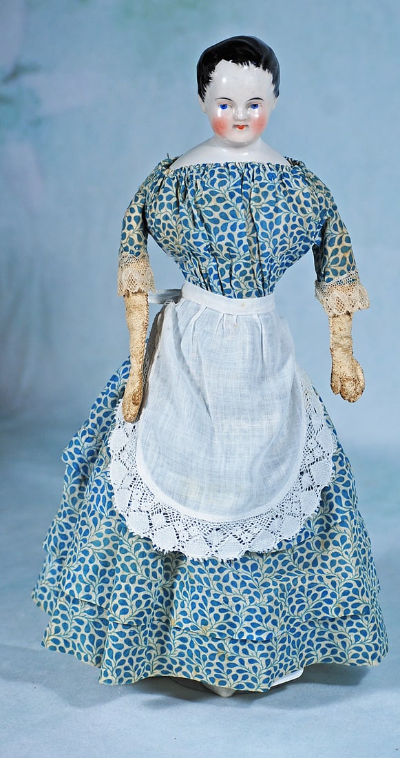 GERMAN PORCELAIN DOLL WITH SCULPTED AND BRUSH-MARKED BLACK HAIR: 14 ½”. Porcelain shoulderhead, sculpted short black hair with stippling detail framing the face, modeled ears, painted features, blue eyes, red and black eyeliner, tapered brows, closed mou