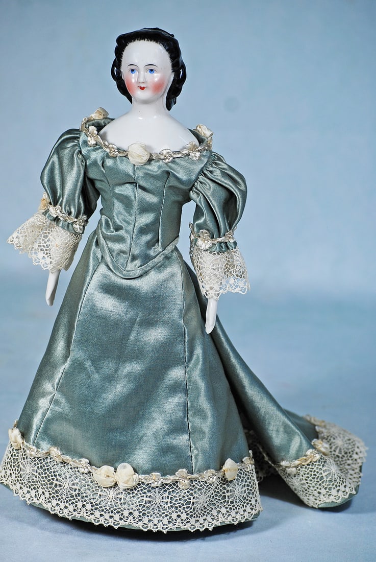 GERMAN PORCELAIN LADY WITH SHOULDER LENGTH HAIR AND SNOOD: 12 ½”. Porcelain shoulderhead, sculpted black hair with stippling detail framing her face, hair waved to the back, arranged in shoulder length curls captured by a black snood, painted featu