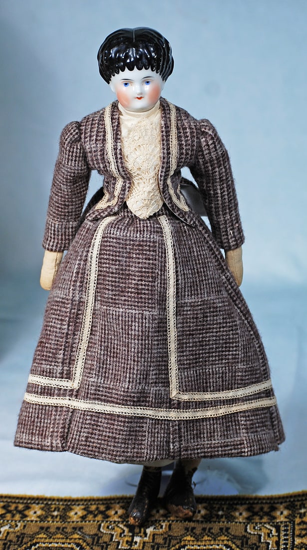 GERMAN PORCELAIN LADY WITH SHORT CURLY HAIR: 15”. Porcelain shoulderhead, deeply defined short curly hair, painted features, shaded blue eyes, red and black eyeliner, tapered brows, closed mouth, old muslin stitch-jointed body with mitten 
