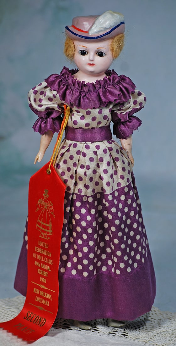 GERMAN WAX OVER PAPER MACHE LADY WITH SCULPTED BONNET: 12 ½”. Wax over papier mache shoulderhead, sculpted lavender bonnet with pink band and plume, blonde mohair around sides and back, large inset dark glass eyes, painted lashes, tapered brows
