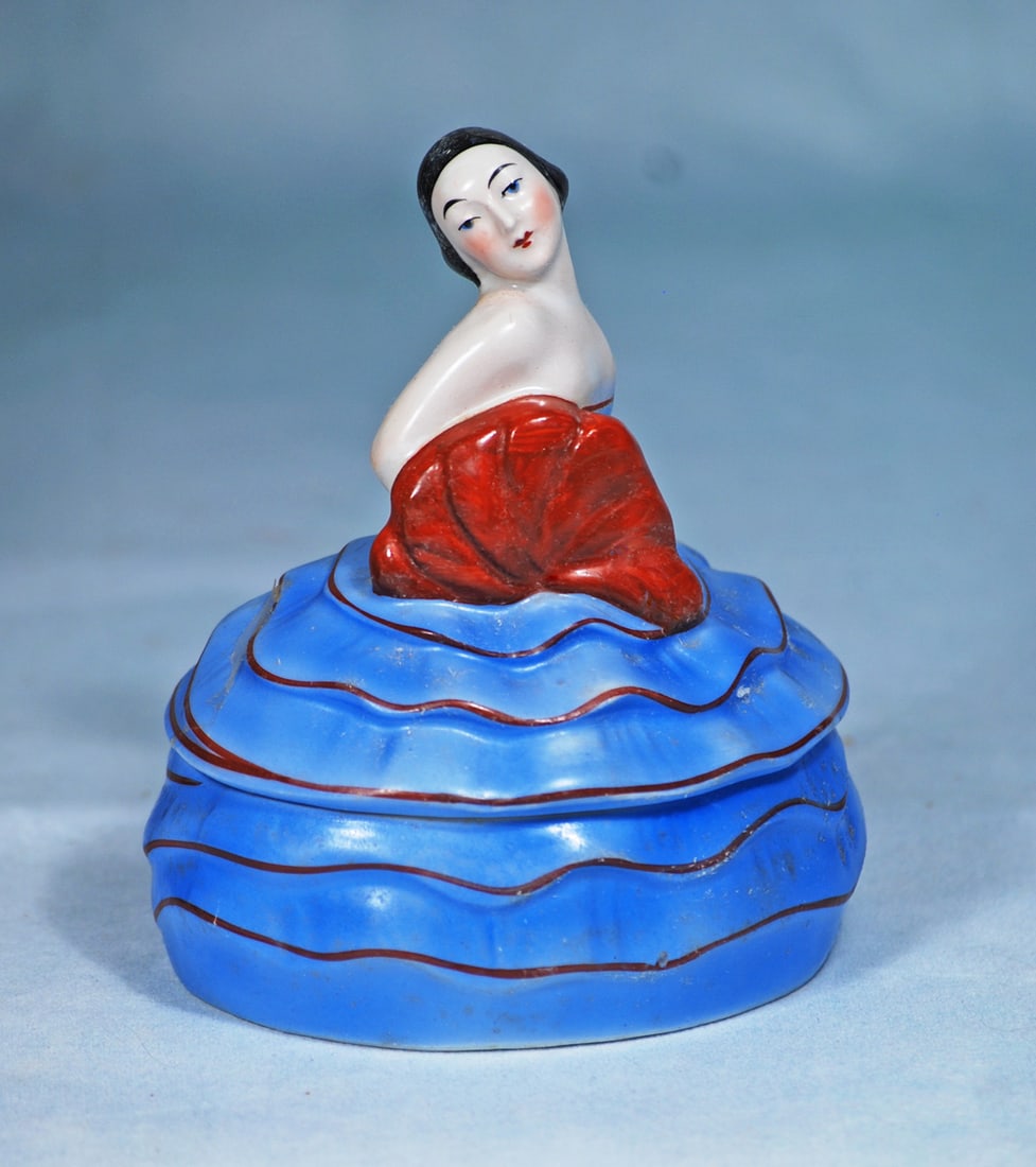 GERMAN PORCELAIN ART DECO POWDER BOX: 5 ½”. Marks: Germany. Two piece porcelain powder box decorated in Art Deco manner in vibrant shaded blue and red colors, features a stylish lady with smooth black hair, head tilted to the s